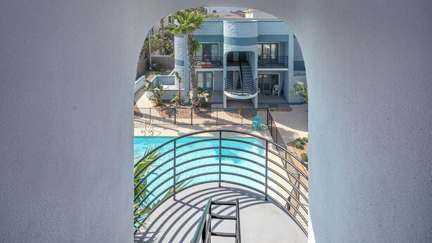 A modern building with a pool, a staircase, and a palm tree. - Dunes #205 | Remodeled Condo • Community Pool • 1 Min Walk to Beach (South Padre Island)