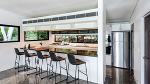 A modern kitchen with a central island, bar stools, a stainless steel refrigerator, and a window overlooking greenery. - Waves 1 Hamilton Island - oceanviews, golf buggy and transfers (Hamilton Island)