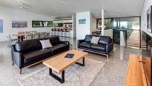 A modern living room with two black leather sofas, a wooden coffee table, and a dining area with a table and chairs. - Waves 1 Hamilton Island - oceanviews, golf buggy and transfers (Hamilton Island)
