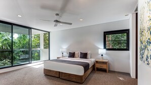 A modern bedroom with a large bed, a ceiling fan, and a view of greenery through large windows. - Waves 1 Hamilton Island - oceanviews, golf buggy and transfers (Hamilton Island)