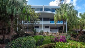 A modern multi-story building with a curved roof, surrounded by lush greenery and tropical plants. - Waves 2 Hamilton Island - oceanviews, golf buggy and transfers (Hamilton Island)
