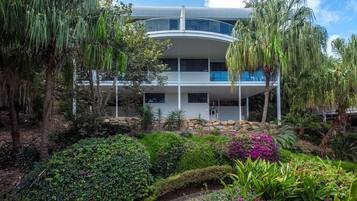 A modern multi-story building with a curved roof, surrounded by lush greenery and tropical plants.