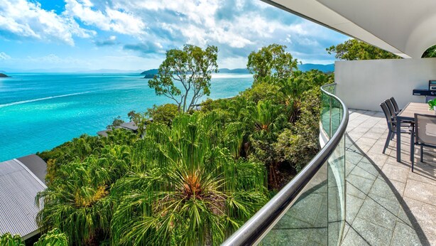 A modern outdoor area with a glass balustrade, a dining table, and chairs. - Waves 2 Hamilton Island - oceanviews, golf buggy and transfers (Hamilton Island)