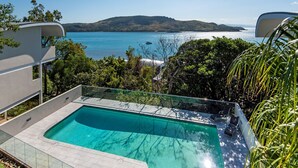 A modern outdoor pool with a glass balustrade, surrounded by lush greenery and overlooking a clear blue sea with distant landforms. - Waves 2 Hamilton Island - oceanviews, golf buggy and transfers (Hamilton Island)
