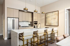 A modern kitchen with a marble island, stainless steel appliances, and bar stools.
