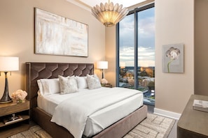 A modern bedroom with a large bed, a city view, a chandelier, and a painting.