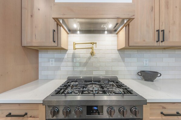 A kitchen with a stainless steel gas stove, wooden cabinets, and a white tiled backsplash. - Beach Glass Retreat - Pickleball, Lake access 2 minute walk away, luxury home (Fennville)