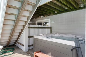 A hot tub in a covered outdoor area with a wooden staircase and a white fence.
