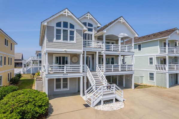 A multi-story beachfront house with balconies, a covered patio, and a clear view of the ocean.