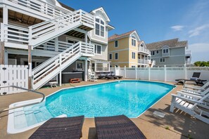A swimming pool with white railings and lounge chairs, surrounded by a white fence and a multi-story building with balconies. - Southern Comfort: Semi-Oceanfront, Private Heated Pool, Elevator, Hot Tub, Dog Friendly! (Nags Head)