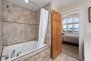 A bathroom with a bathtub, shower, and wooden door leading to a bedroom.