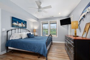 A bedroom with a bed, a ceiling fan, a painting, a TV, and a dresser.