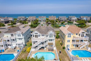 A coastal residential area with multiple two-story houses featuring balconies, a swimming pool, and a view of the ocean.