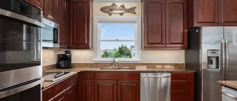 A kitchen with wooden cabinets, stainless steel appliances, a dishwasher, and a window with a view of the outside.