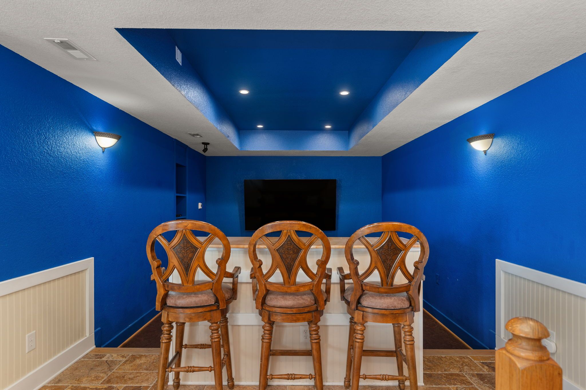 Une pièce aux murs bleus, avec un téléviseur à écran plat fixé au mur et trois chaises en bois dotées d’assises rembourrées.