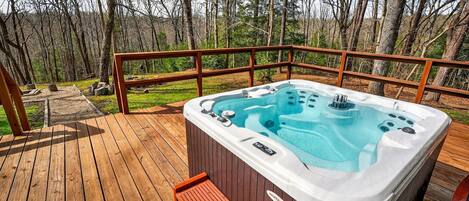 Ein Whirlpool auf einer Holzterrasse mit Geländer, umgeben von Bäumen.