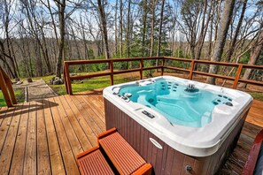 A hot tub on a wooden deck with a railing, surrounded by trees. - Lazy Lane Cabins - Bobcat Hideaway (South Bloomingville)
