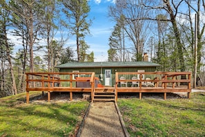 Une cabane avec une terrasse en bois, un porche couvert et un petit abri de jardin.