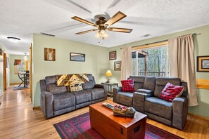 A living room with two grey sofas, a wooden coffee table, a ceiling fan, and a window with curtains.