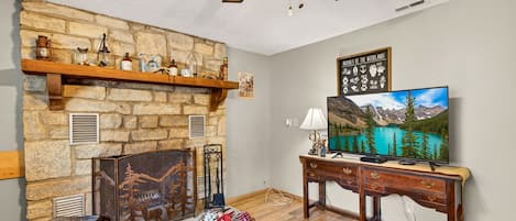 Un salon avec une cheminée en pierre, un téléviseur et une table basse en bois.