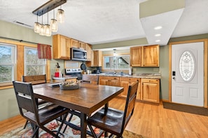 A kitchen with wooden cabinets, a dining table with chairs, a microwave, and a stove. - Lazy Lane Cabins - Bobcat Hideaway (South Bloomingville)