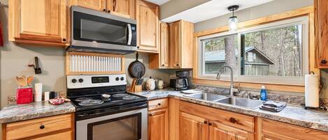 Una cocina con armarios de madera, una estufa de acero inoxidable, un microondas, un fregadero y una ventana con vistas a una construcción de madera.