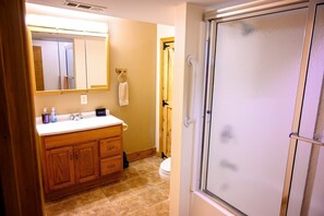 A bathroom with a wooden vanity, a mirror, a toilet, and a shower door. - Lazy Lane Cabins - Moonlight Ridge (Laurelville)