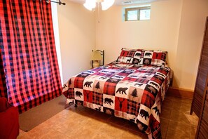 A bedroom with a checkered bedspread, a lamp, a window, and a door.