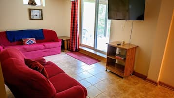 A living room with a red sofa, a television mounted on the wall, and a window with curtains.