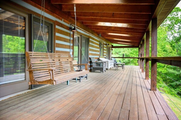 A wooden deck with a bench and chairs, a table, and a hanging light fixture.