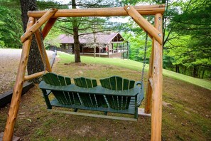 A wooden swing set with a bench seat, a tree, and a cabin in the background. - Lazy Lane Cabins - Moonlight Ridge (Laurelville)