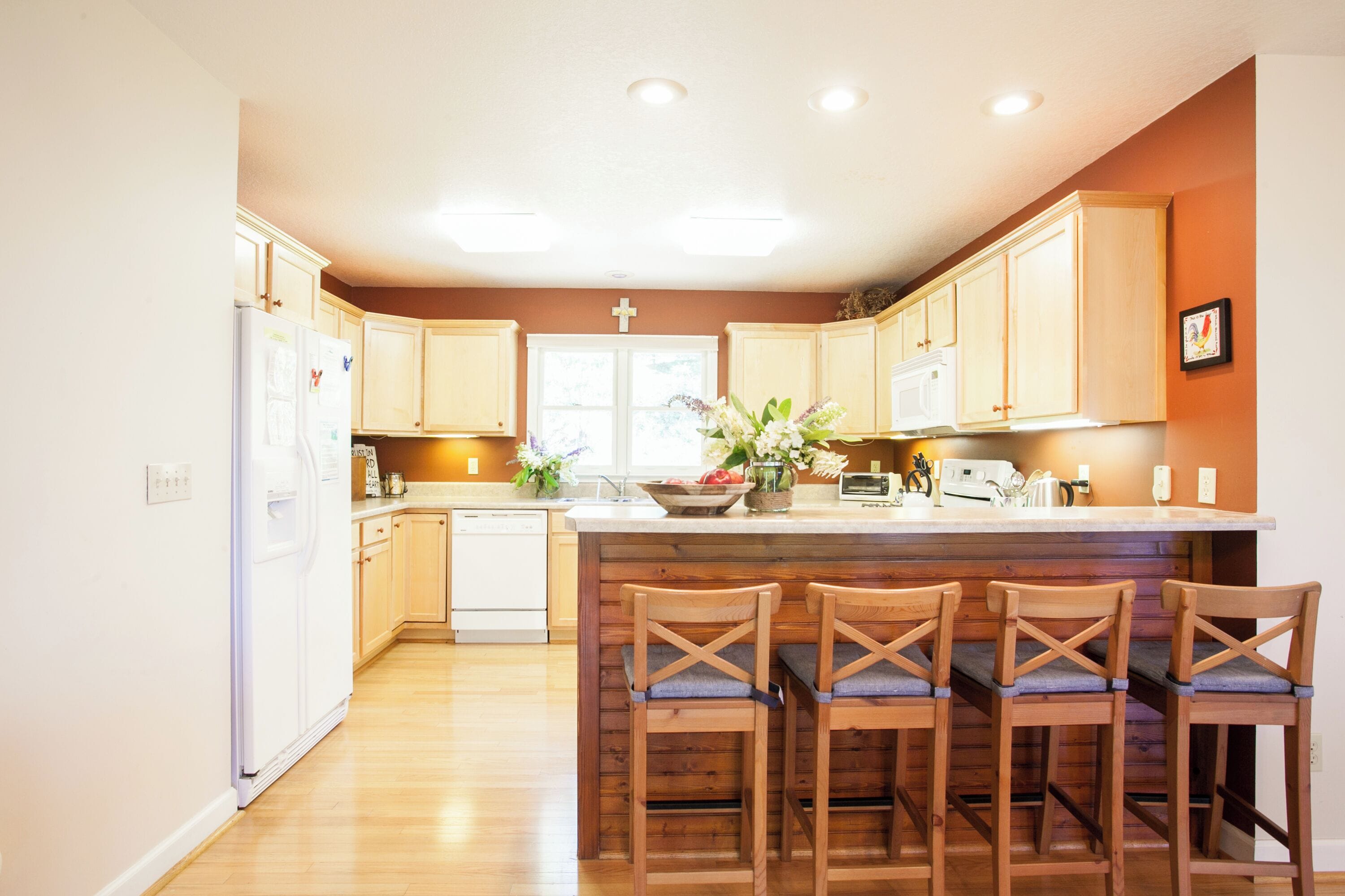 A kitchen with wooden cabinets, a white refrigerator, and a bar area with wooden stools.