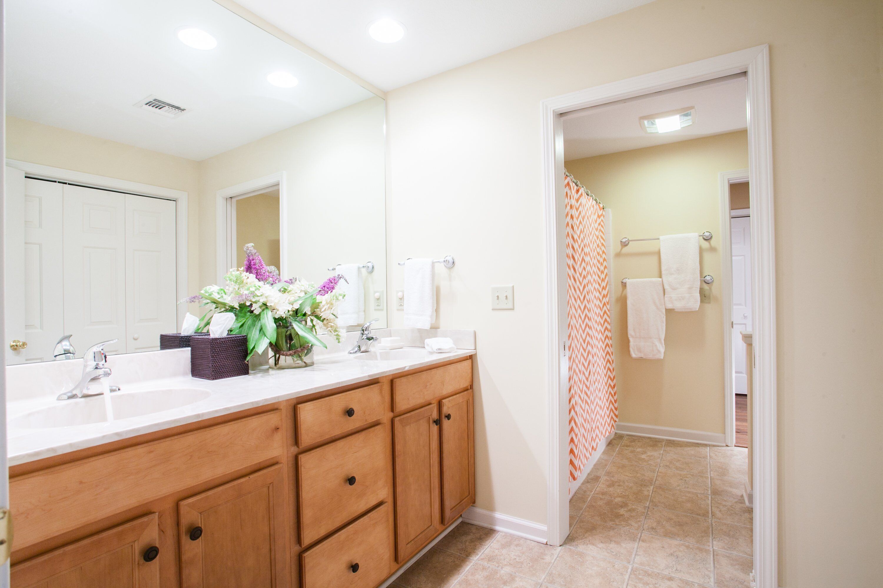 A bathroom with a wooden vanity, a large mirror, a sink, and a shower area with a patterned shower curtain.