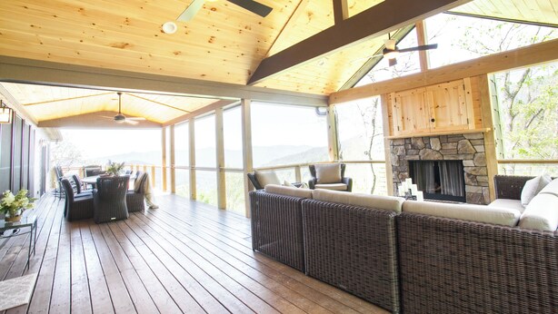 Une terrasse couverte, meublée de mobilier en osier, avec une cheminée en pierre et une vue sur l’extérieur.