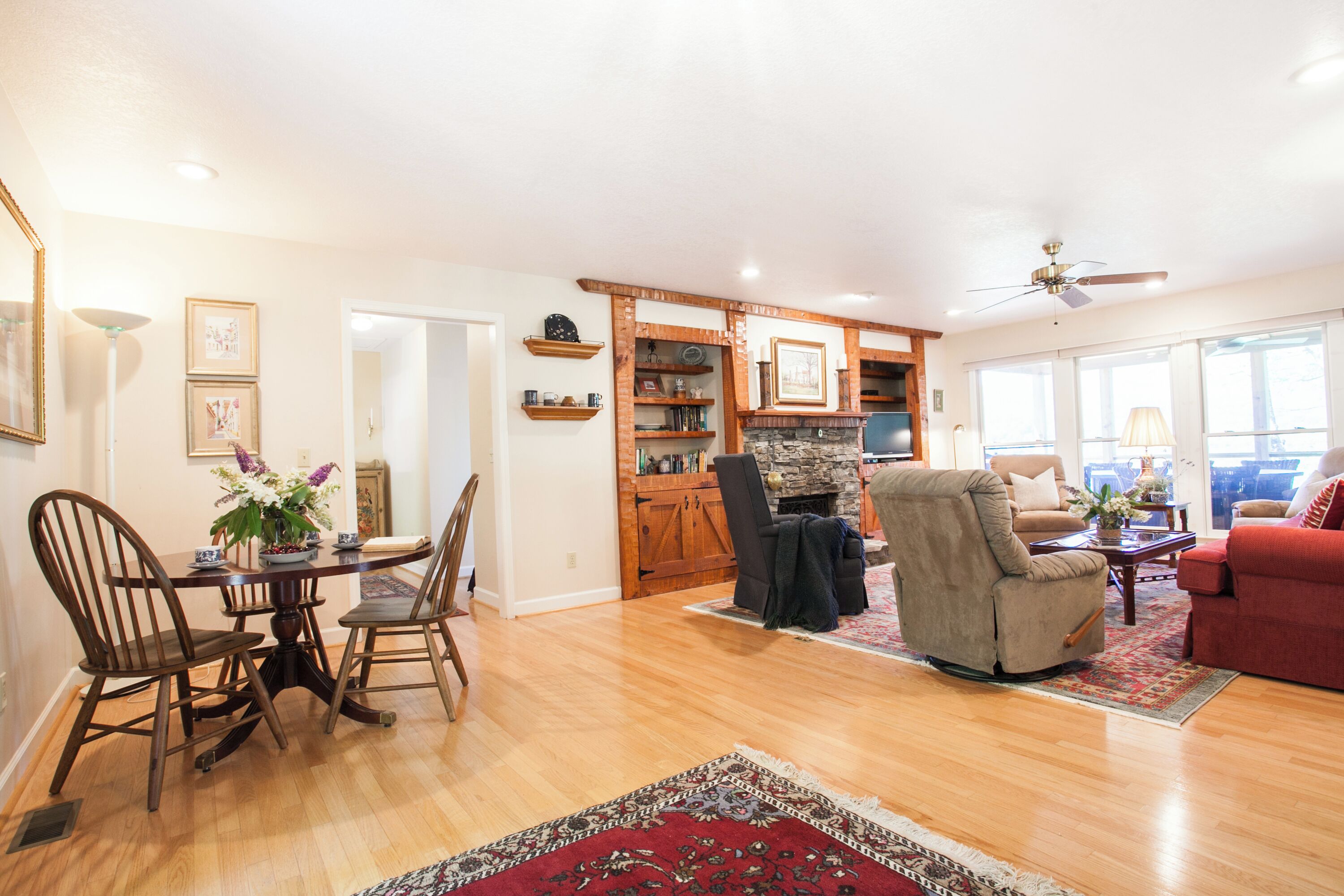 A spacious living room with a fireplace, a dining area with wooden chairs, and a red sofa.