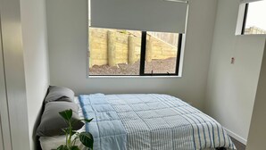 Ein kleines, ordentlich eingerichtetes Schlafzimmer mit einem Einzelbett, einem Blumentopf und einem Fenster mit Blick auf einen Holzzaun.