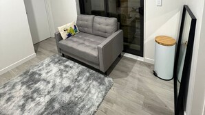 Ein modernes Wohnzimmer mit einem grauen Sofa, einem flauschigen Teppich und einem kleinen runden Tisch.