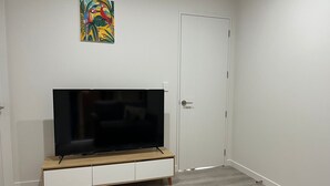 Ein Zimmer mit einem Flachbildfernseher auf einem hölzernen TV-Schrank, einer weißen Tür und einem farbenfrohen Gemälde an der Wand.