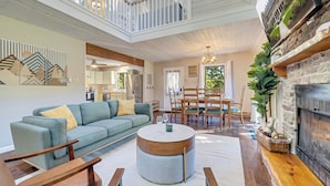 A spacious living room with a high ceiling, a fireplace, and a dining area. - New! Hot Tub, Fire-pit, Shuffleboard, Games Room, Kids Area in Gated Community (Albrightsville)