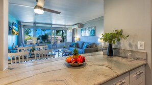 Una cocina moderna con encimera de mármol, frutero y zona de comedor con mobiliario blanco.