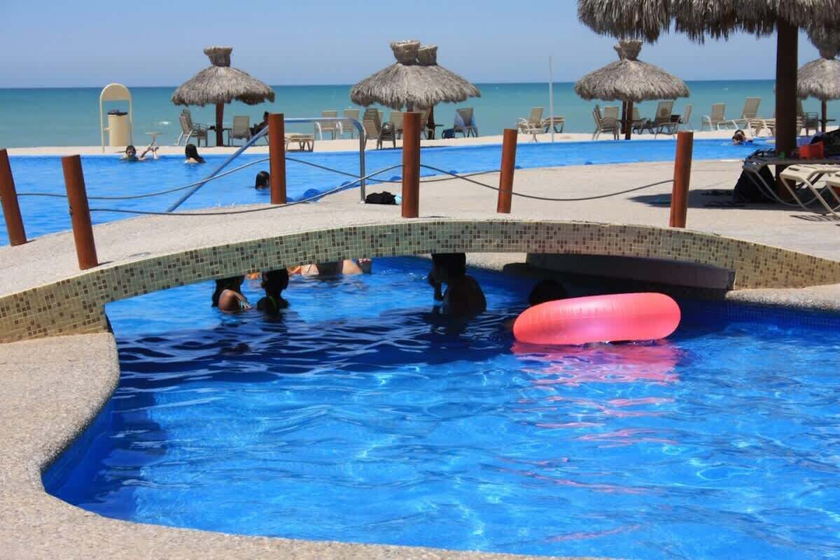 A swimming pool with a bridge, lounge chairs, and thatched umbrellas.