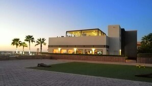 A modern building with a flat roof, large windows, and a paved area with palm trees. - Seaside Hacienda, Laguna Shores Resort, 6 Bedroom (Puerto Peñasco)