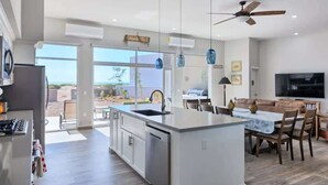 A modern kitchen with a central island, dining area with chairs, and a large TV.