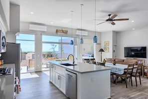 Enjoy a spacious open-plan living area with a central kitchen, dining space, and large windows offering a view of the surrounding landscape.