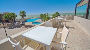 A rooftop terrace with a pool, palm trees, and a view of the sea.