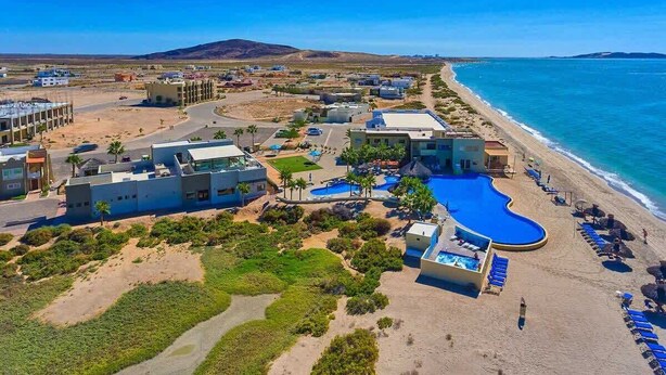 An aerial view of a coastal resort with multiple buildings, a swimming pool, and a beach.