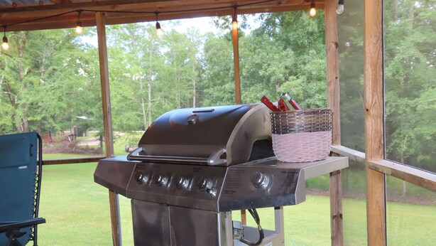 Un espace extérieur abrité comprenant un barbecue en acier inoxydable, une chaise pliante bleue et une table avec un panier.