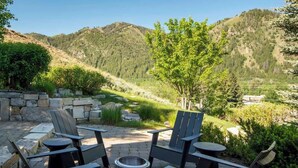 An outdoor seating area with Adirondack chairs and a metal fire pit, surrounded by stone walls and a view of a mountainous landscape. - Abode at Sunny Knob Hill, scenic setting, hot tub (Ketchum)