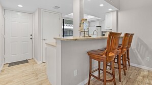A kitchen with a bar area, wooden chairs, and a white door. - Bonita Bay Condo, Beach Club Included! Corner unit! (Bonita Springs)