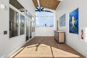 A spacious room with large windows, a wooden floor, and a wall-mounted fire extinguisher.
